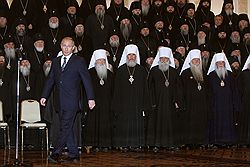 Президент России Владимир Путин (в центре) не смог усидеть на месте в присутствии всех иерархов церкви. Загружается с сайта Ъ